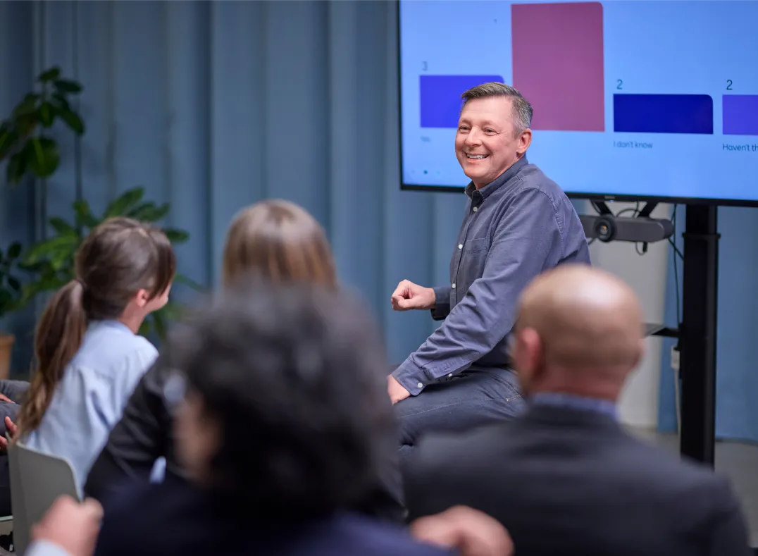 Crowed of people watching a smiling man sitting in front of a bar chart presentation
